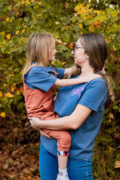 Woman holding a child in an outdoor setting with trees and leaves.